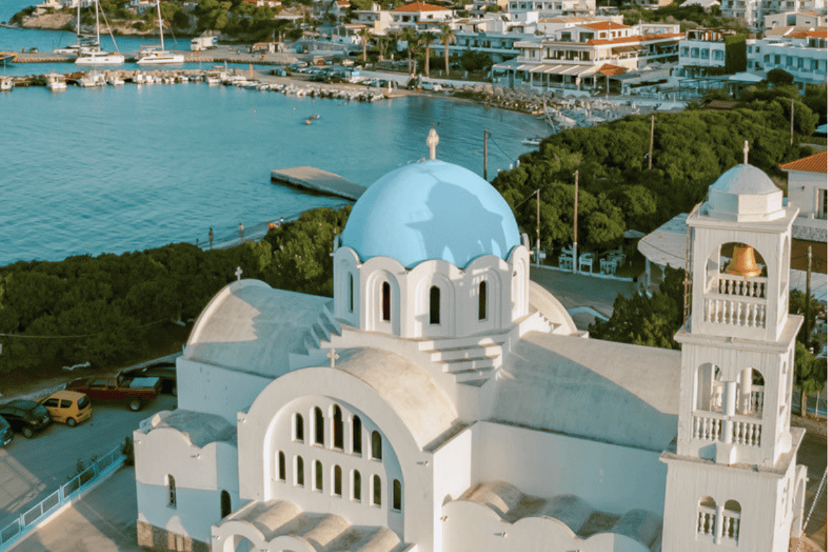 Blue domed church and bell tower overlooking the turquoise sea and harbor on Agistri, one of the sights to see when exploring things to do in Agistri.