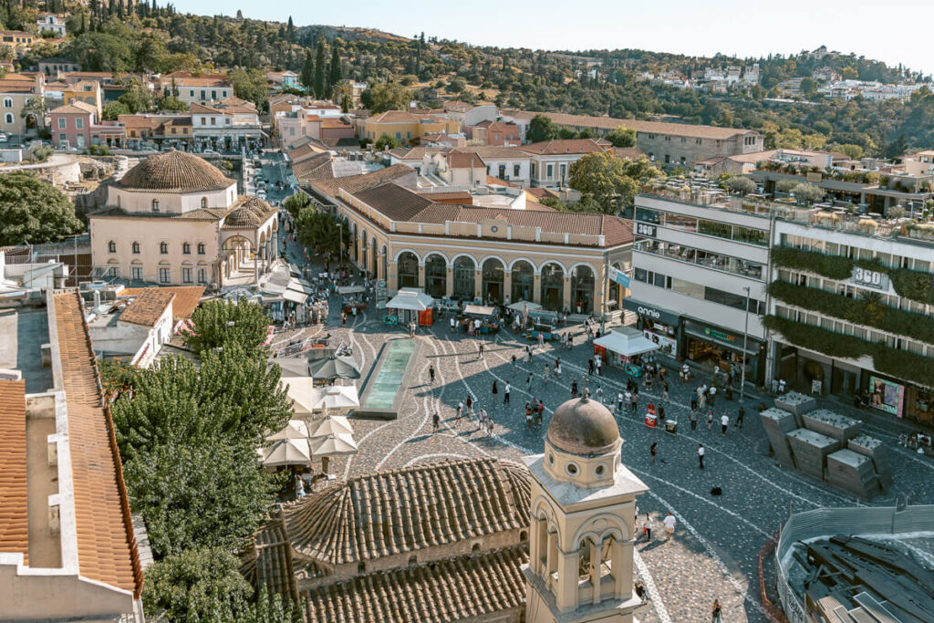 Aerial view of Monastiraki Square in Athens with crowds walking through historic streets, market stalls, and surrounding buildings, capturing the vibrant energy of the city.