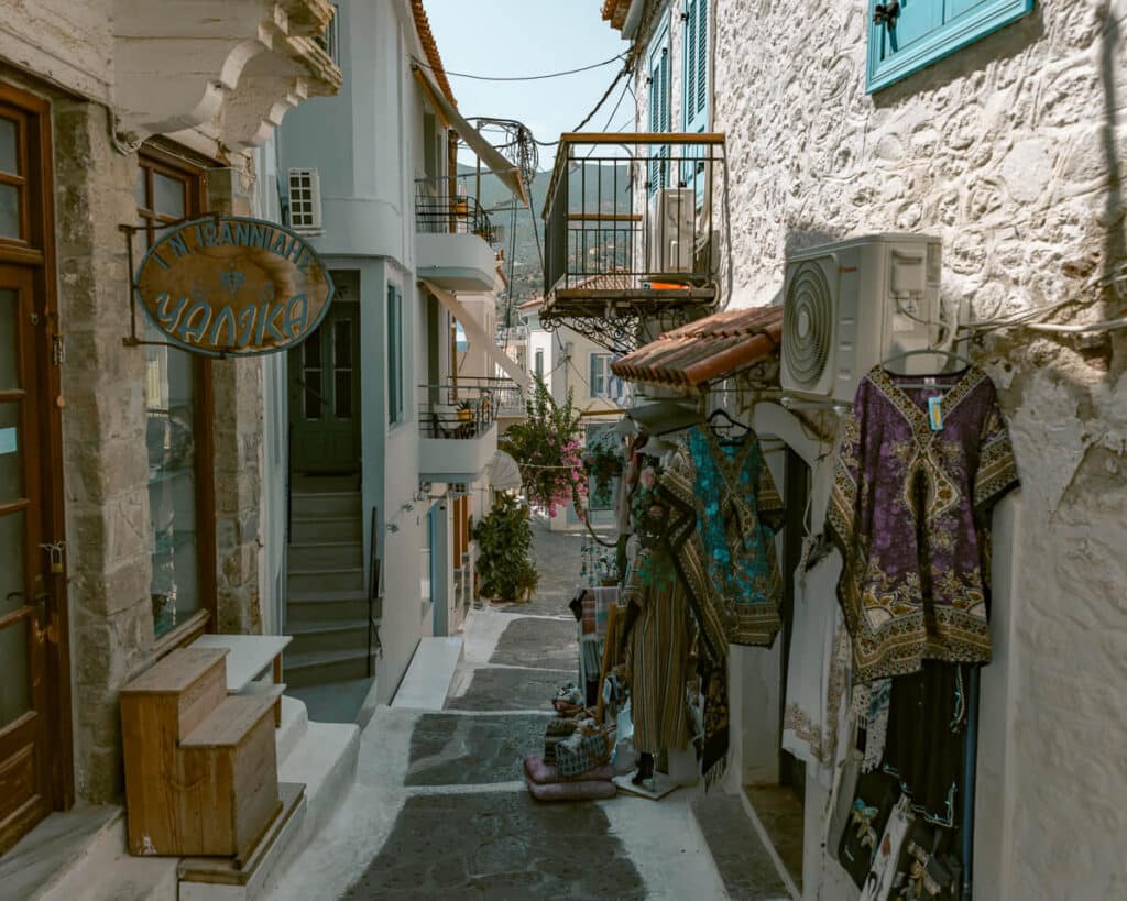 Small shopping street in Poros with whitewashed buildings, balconies, and dresses hanging outside a local boutique, showing island shopping and daily life.