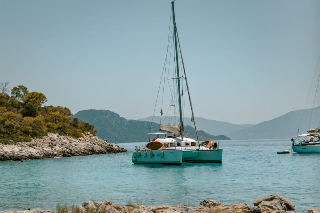 Catamaran anchored in clear blue water near a rocky Greek shoreline in Agistri, highlighting the calm seas and scenic coastlines travelers experience when visiting Greek islands.