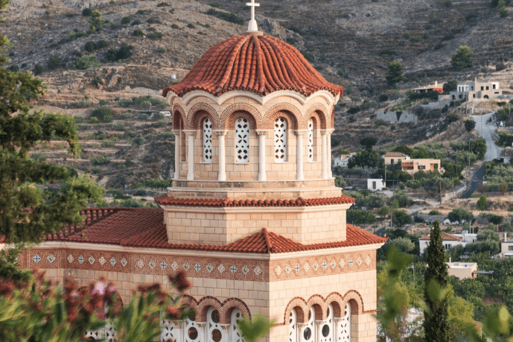 Monastery of Agios Nektarios with a red tiled roof and stone arches, set against a dry hillside in Aegina, Greece, showing traditional island architecture during a day trip to Aegina.