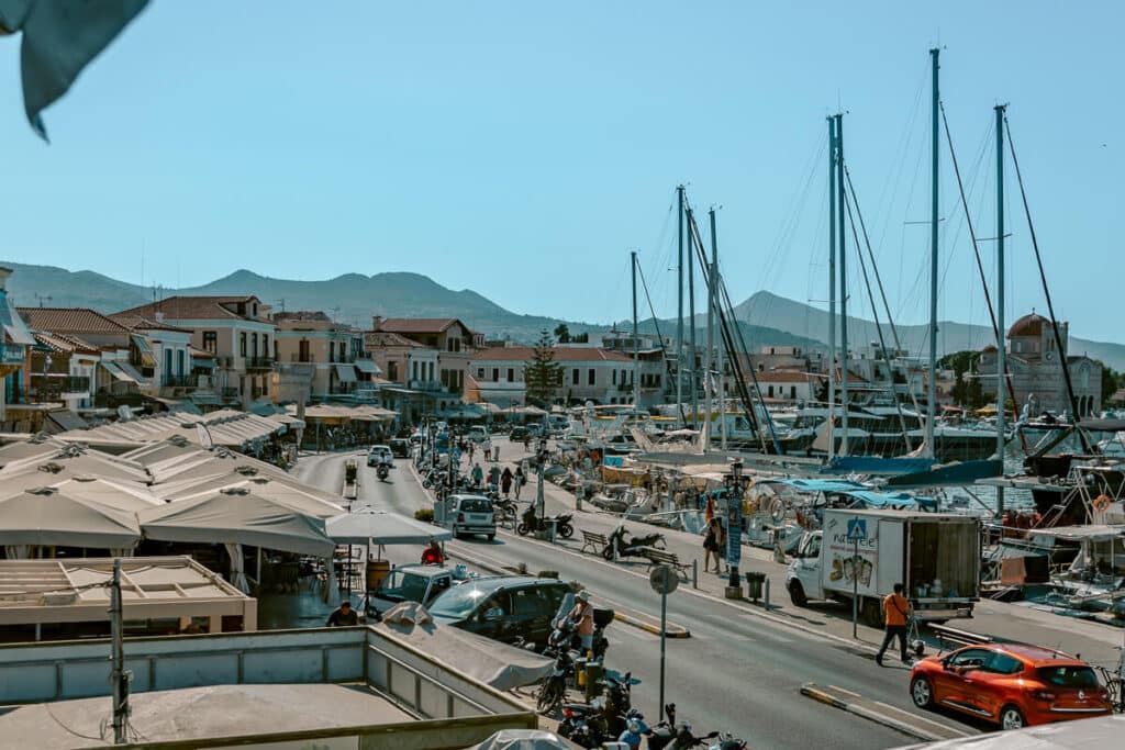 View of Aegina harbor with boats, cafés, and waterfront buildings under a clear sky, illustrating the main arrival point.