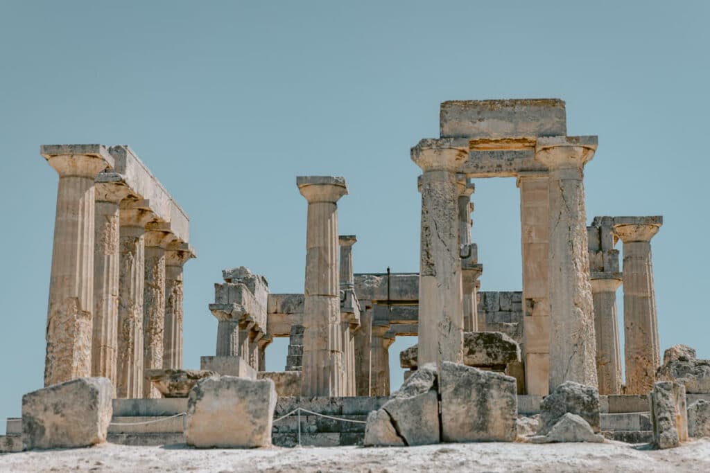 Ruins of the Temple of Aphaia with weathered columns and stone blocks, set on a hilltop in Aegina, Greece, overlooking the surrounding landscape.