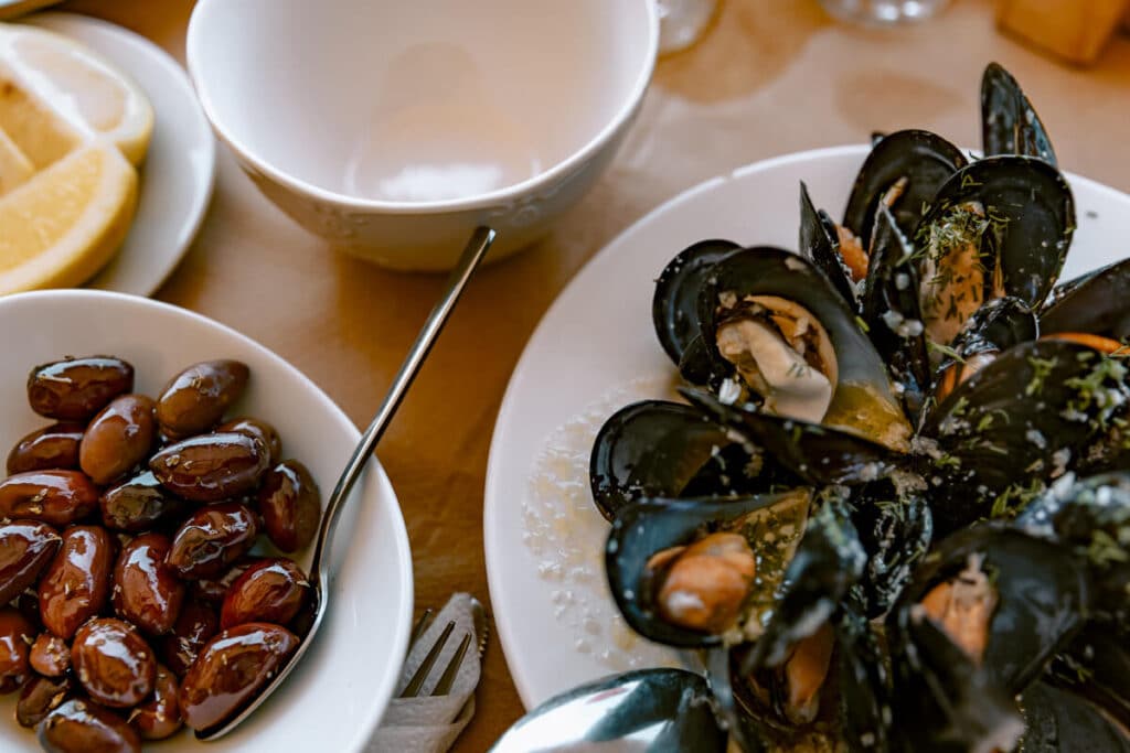 Plates of Greek seafood including mussels, olives, and lemon served on a table, representing traditional Greek food.