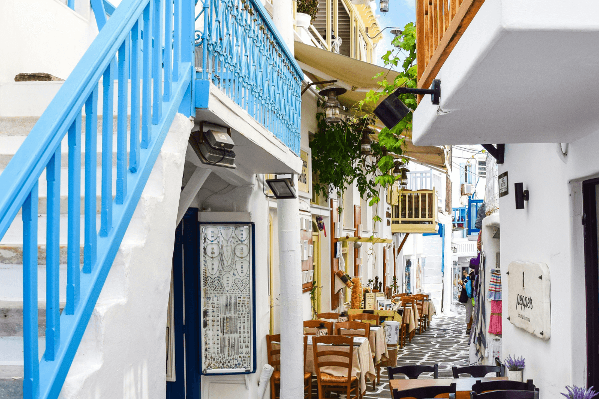 Colorful alley in Mykonos with blue staircase, whitewashed walls, and seaside taverna seating on one of the best Greek islands to visit for the first time.