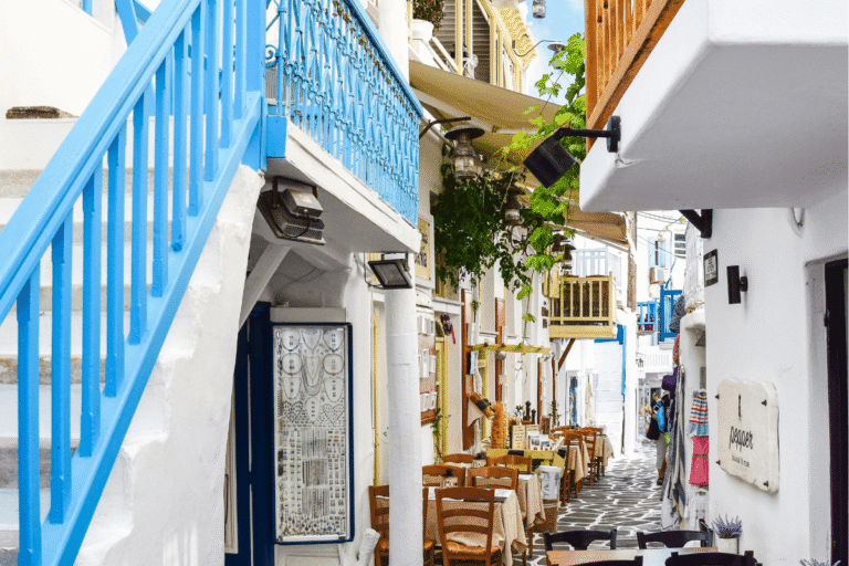 Charming Greek island alley with whitewashed buildings, blue railings and traditional tavernas, highlighting helpful Greece travel tips for your trip.