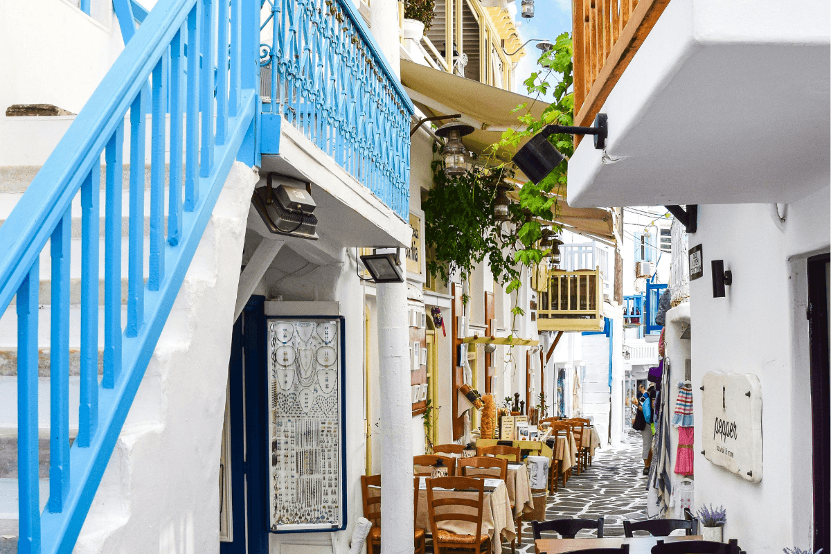 Charming Greek island alley with whitewashed buildings, blue railings and traditional tavernas, highlighting helpful Greece travel tips for your trip.