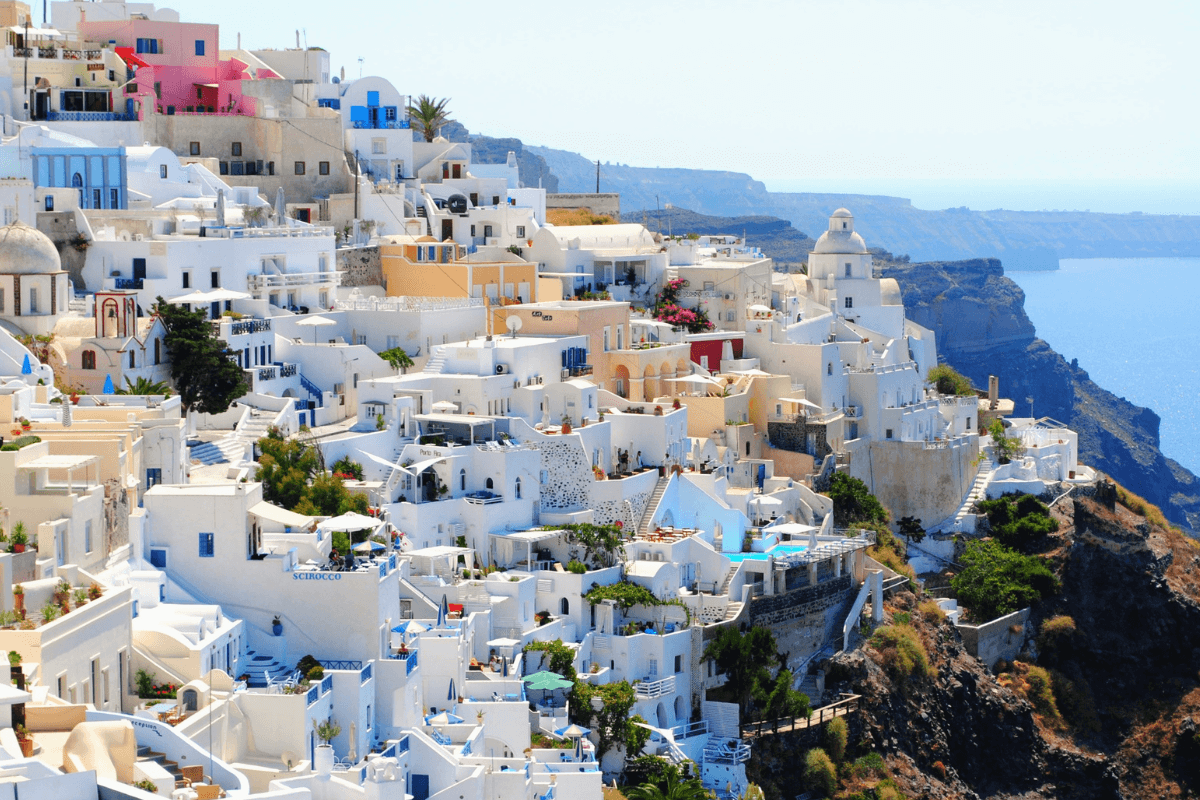 Whitewashed buildings with colorful accents along the dramatic caldera cliffs, a classic Santorini setting to consider when planning what to wear in Santorini.