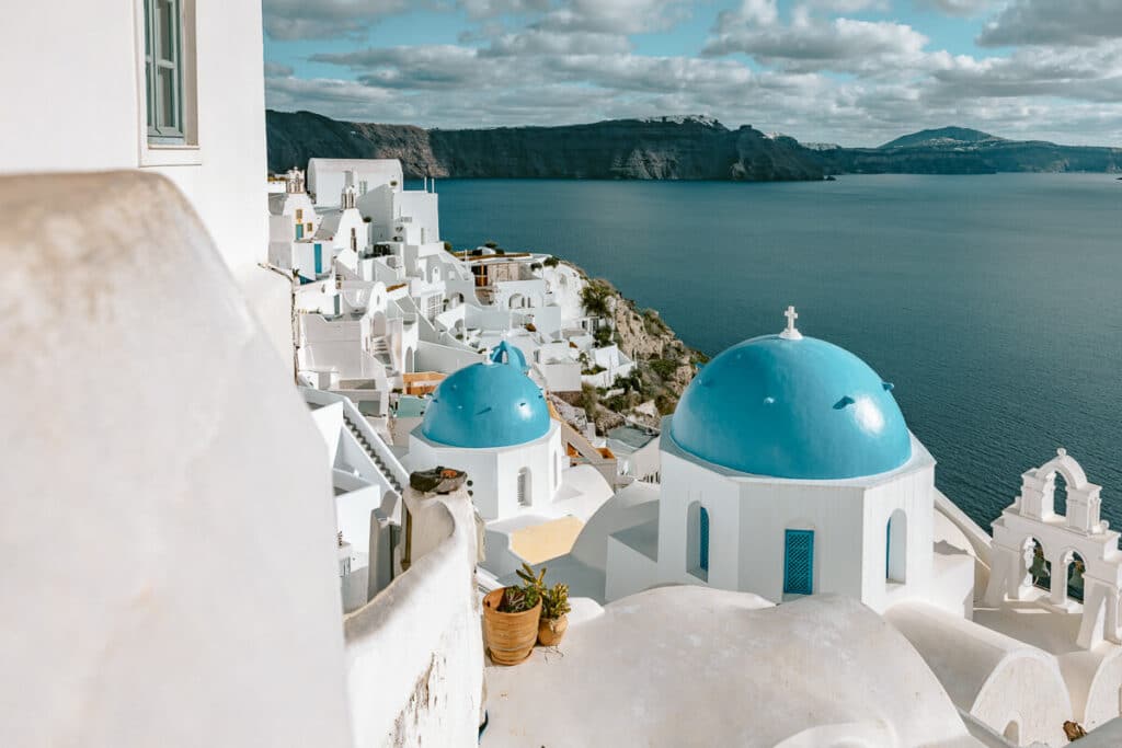 Santorini caldera view with whitewashed buildings and blue domes overlooking the sea under a cloudy sky.