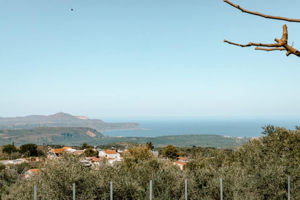 Wide view over olive groves, village rooftops, and the sea near Chania, showing the scenic countryside around western Crete