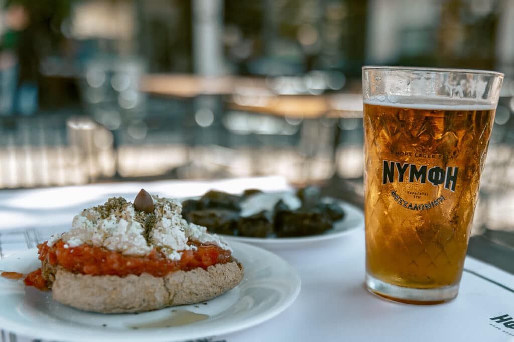 Glass of beer with dakos and small dishes on a table in Chania, capturing the local food and drink scene in Crete