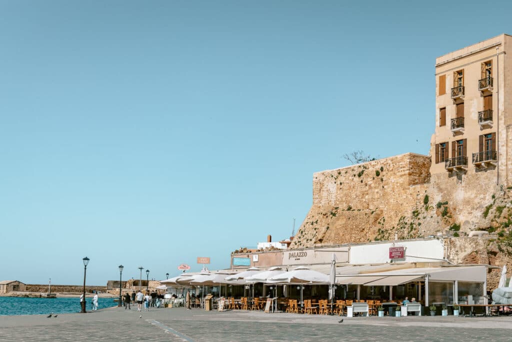 Waterfront promenade in Chania with seaside restaurants, stone walls, and the Venetian harbor under a clear blue sky