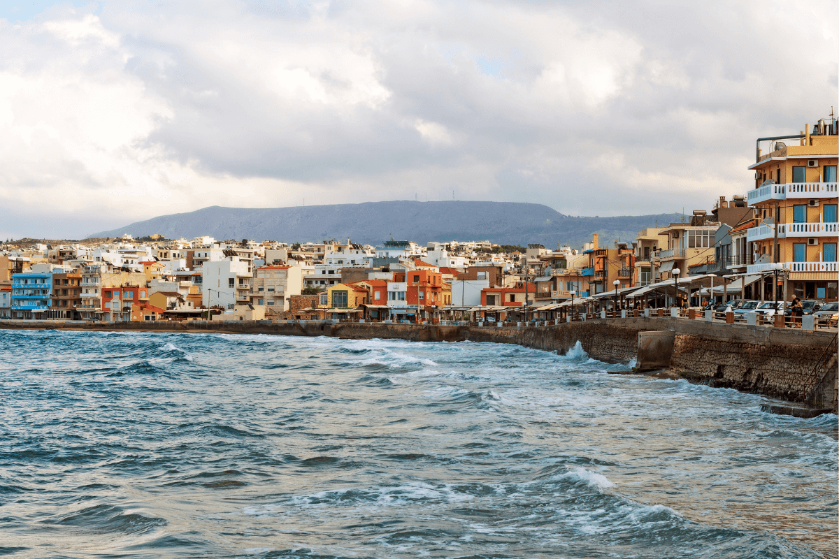 Waterfront view of Chania, Crete, with waves, colorful buildings, and cloudy skies along the coast during a trip focused on things to do in Chania.