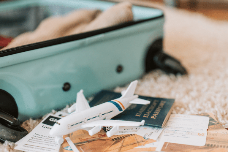 Open suitcase with a passport, plane model, travel tickets, and essentials laid out for an Athens packing list.