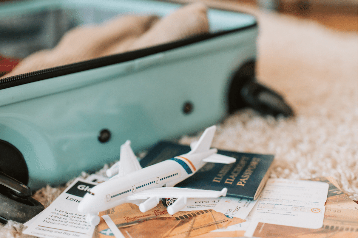 Open suitcase with a passport, plane model, travel tickets, and essentials laid out for an Athens packing list.