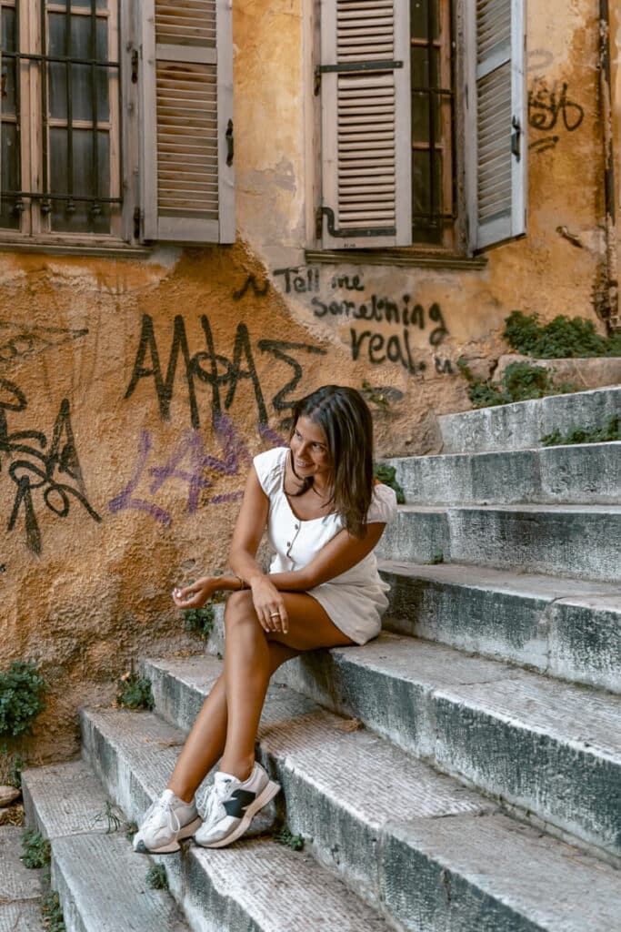 Me wearing a white dress and comfortable sneakers while sitting on stone steps in Athens, showing a practical outfit for walking around the city.