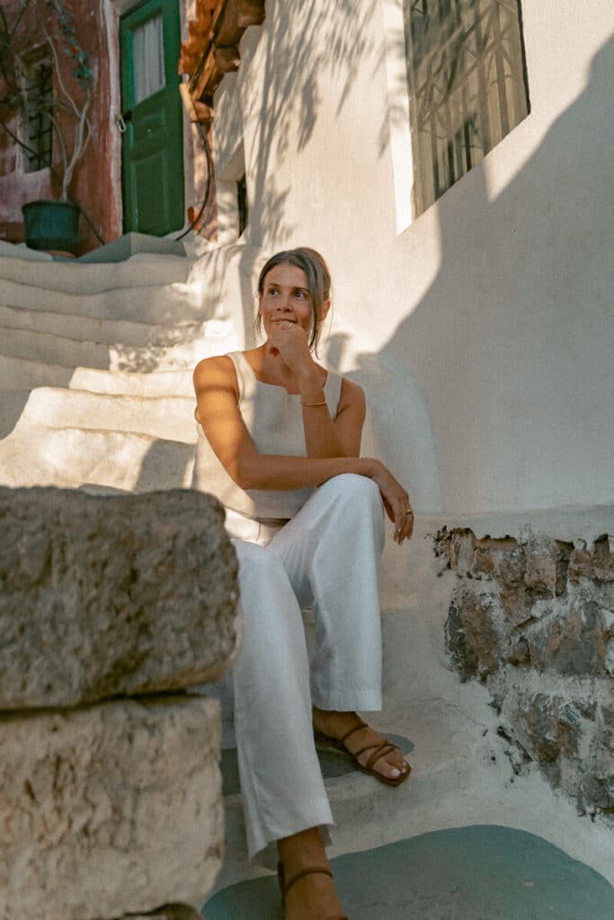Me wearing a sleeveless top, white pants, and flat sandals while sitting on stone steps in Athens.