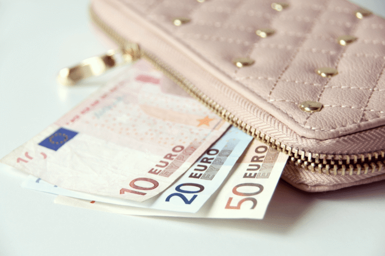 Euro banknotes beside a pink wallet showing travel costs for visitors wondering is Greece expensive.