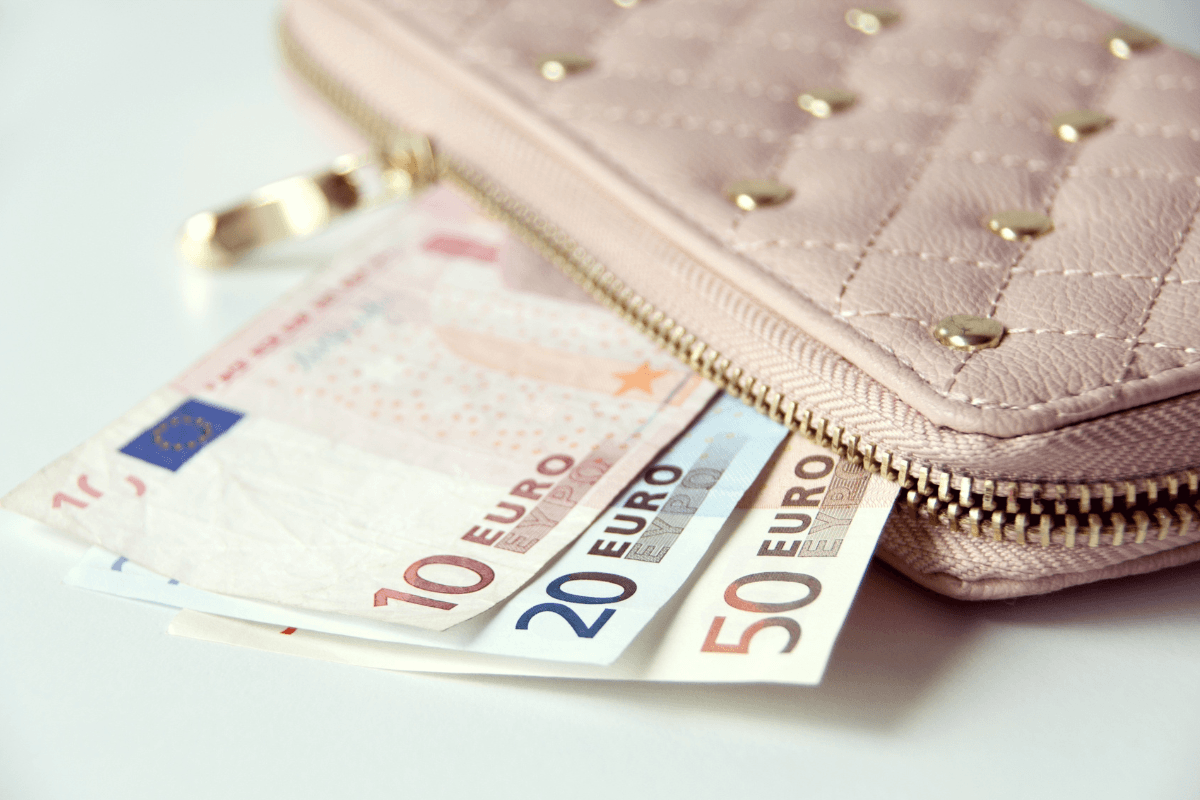 Euro banknotes beside a pink wallet showing travel costs for visitors wondering is Greece expensive.