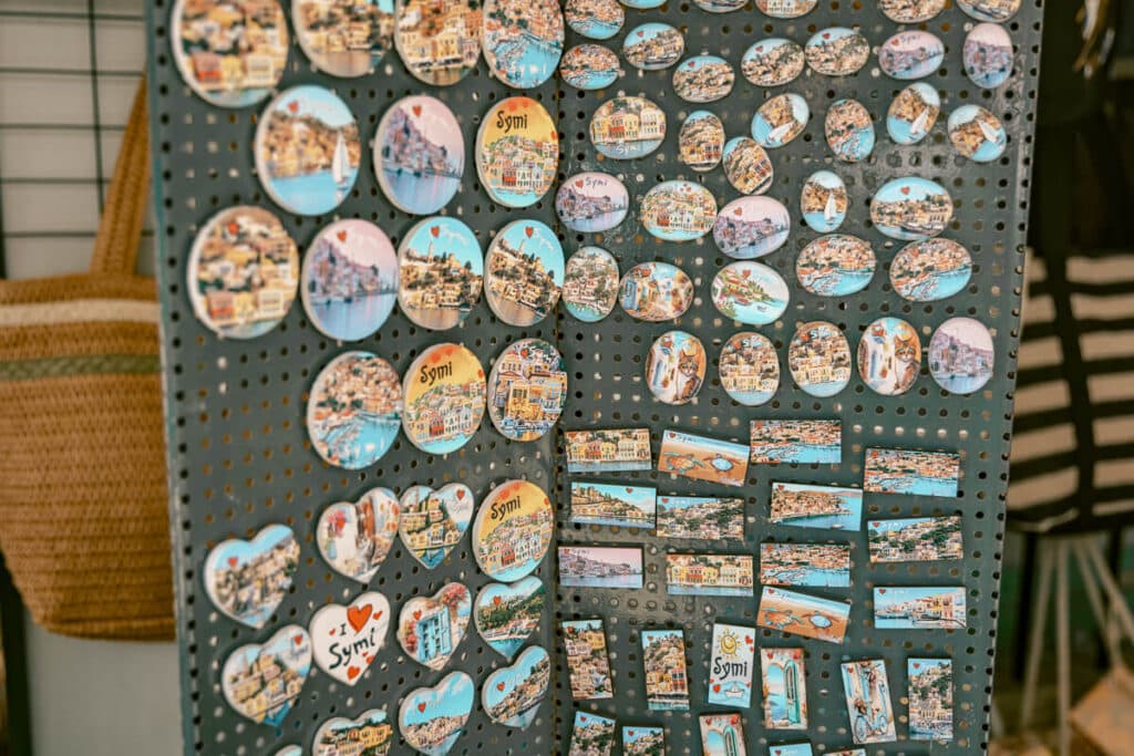 Display of colorful Symi souvenir magnets showing the island’s harbor, pastel houses, boats, and Greek island scenes inside a local shop.
