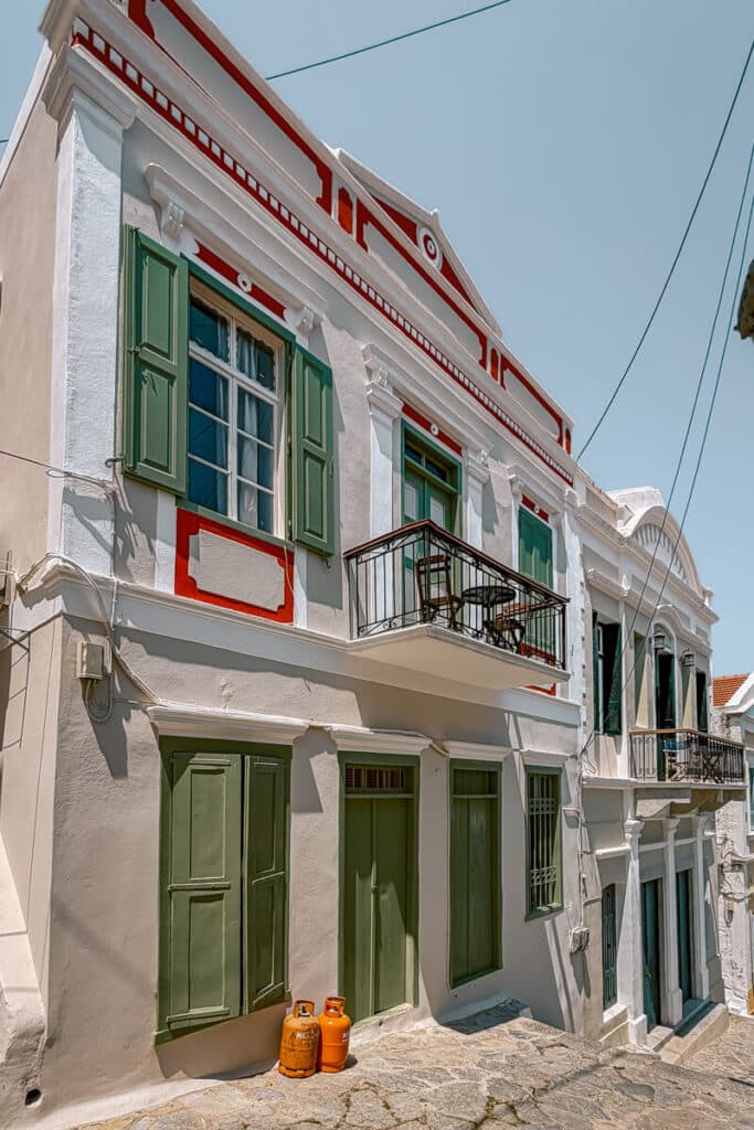 White neoclassical homes in Symi with green shutters, red trim, small balconies, and a stone walkway in the quiet hillside streets.