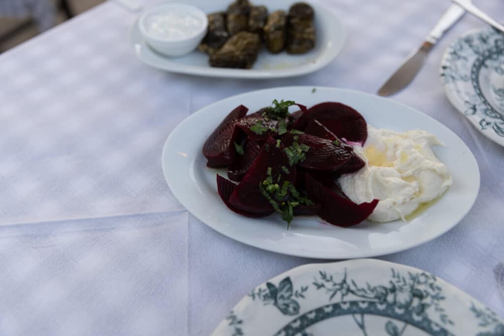 Plate of sliced beets with creamy skordalia on a white tablecloth, with dolmades served in the background at a restaurant in Rhodes.