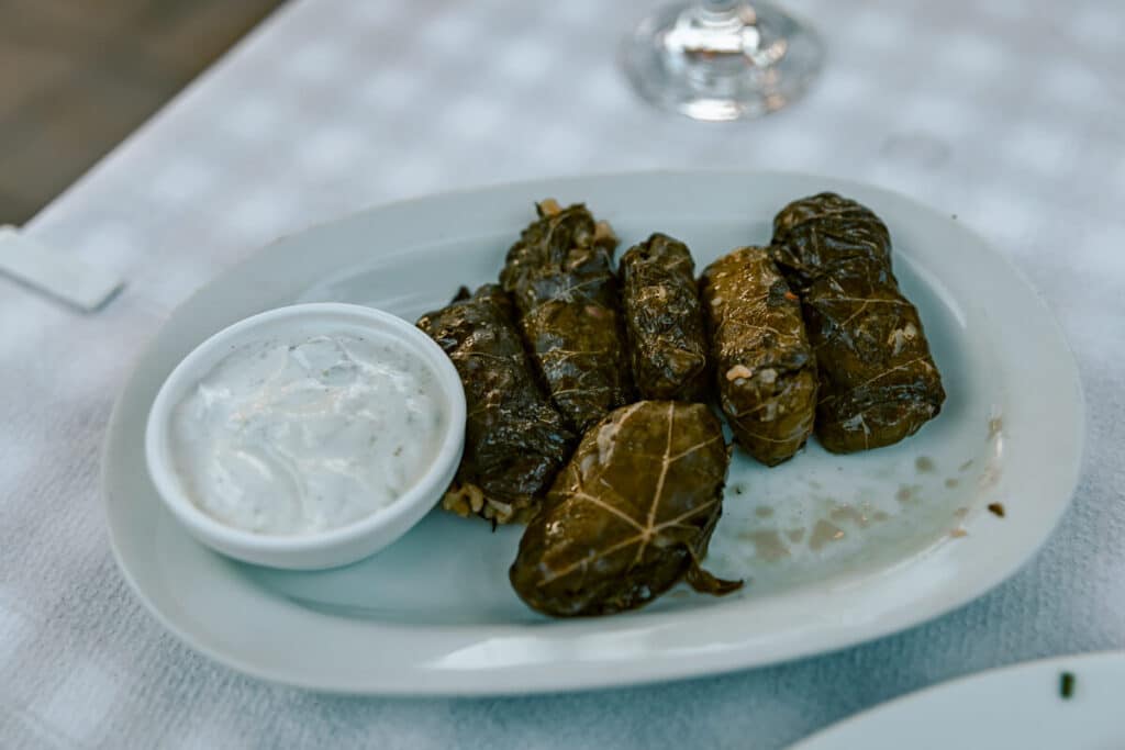 Plate of dolmades served with a small bowl of creamy yogurt sauce on a white tablecloth at a restaurant in Rhodes.