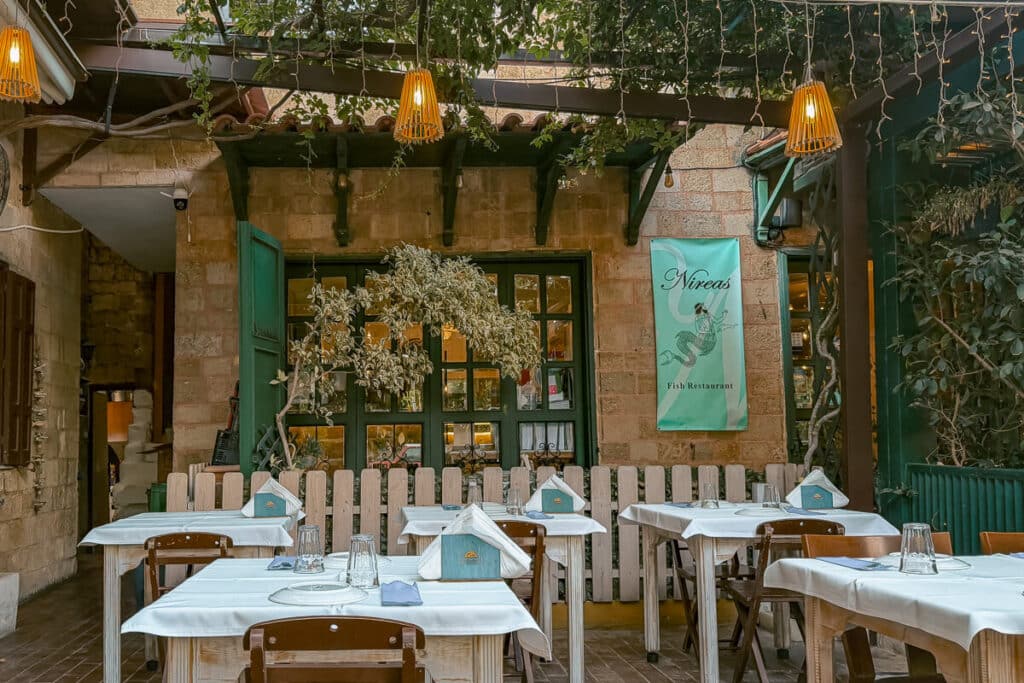 Outdoor seating at Nireas Fish Restaurant in Rhodes Old Town, with white tablecloths, stone walls, greenery, and warm hanging lights.