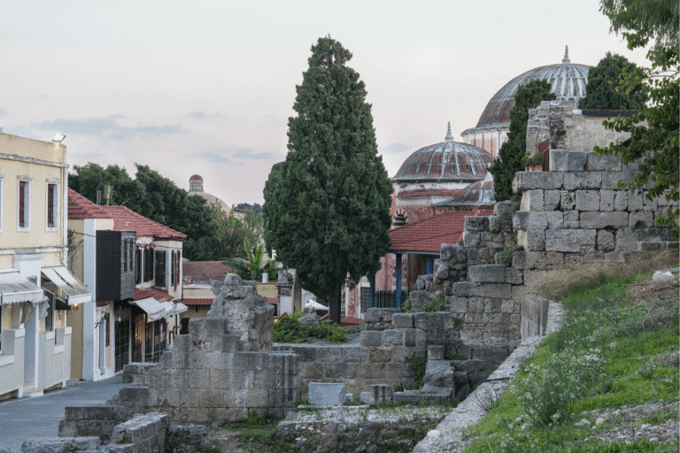Rhodes travel guide featured photo showing stone ruins, narrow streets, trees, and domed historic buildings in Rhodes Old Town, Greece.