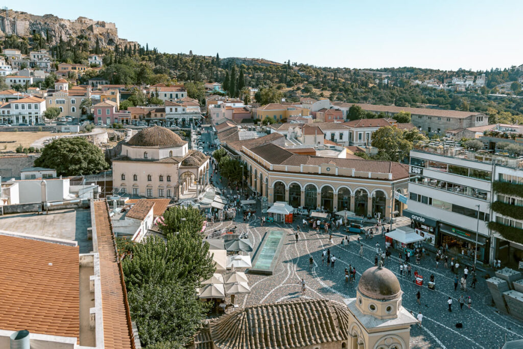 View over Monastiraki Square in Athens, with the Tzistarakis Mosque, busy pedestrian streets, red rooftops, and the Acropolis rising in the background.