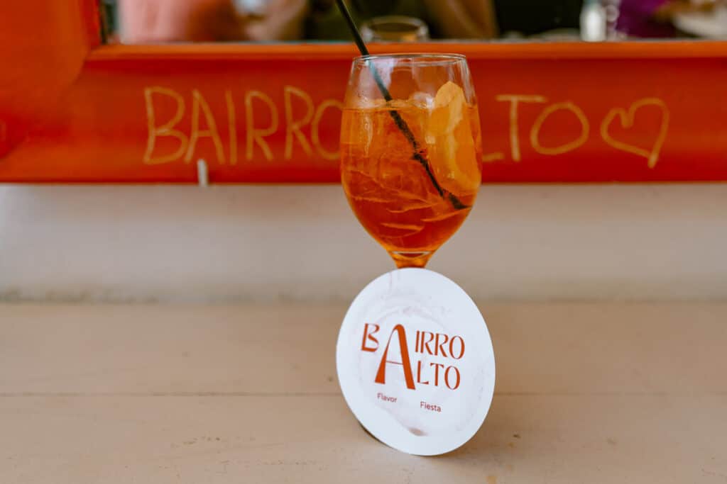 Orange cocktail served at Bairro Alto in Paxos with the bar name written on the wall behind the glass.