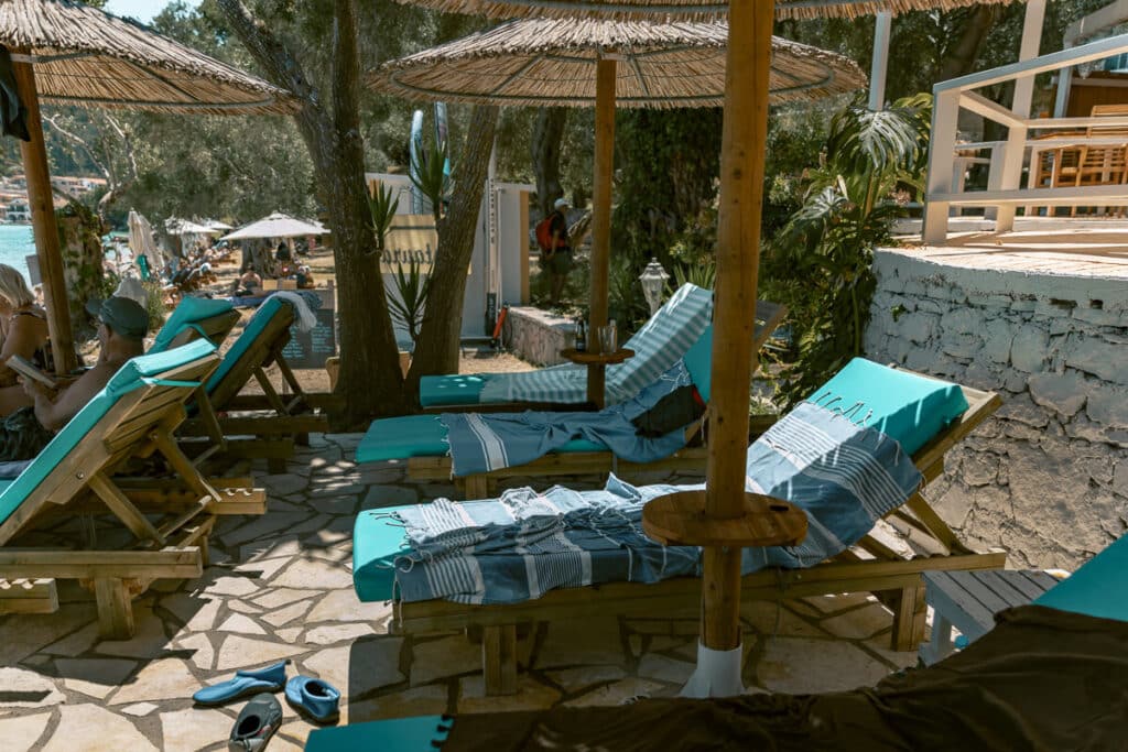 Beach club sunbeds with turquoise cushions and straw umbrellas beside the water in Paxos.