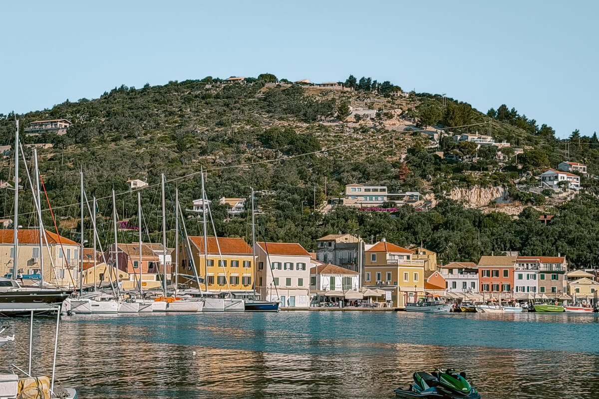 Paxos travel guide featured image showing colorful waterfront buildings, sailboats, and a green hillside behind the harbor in Gaios, Paxos.