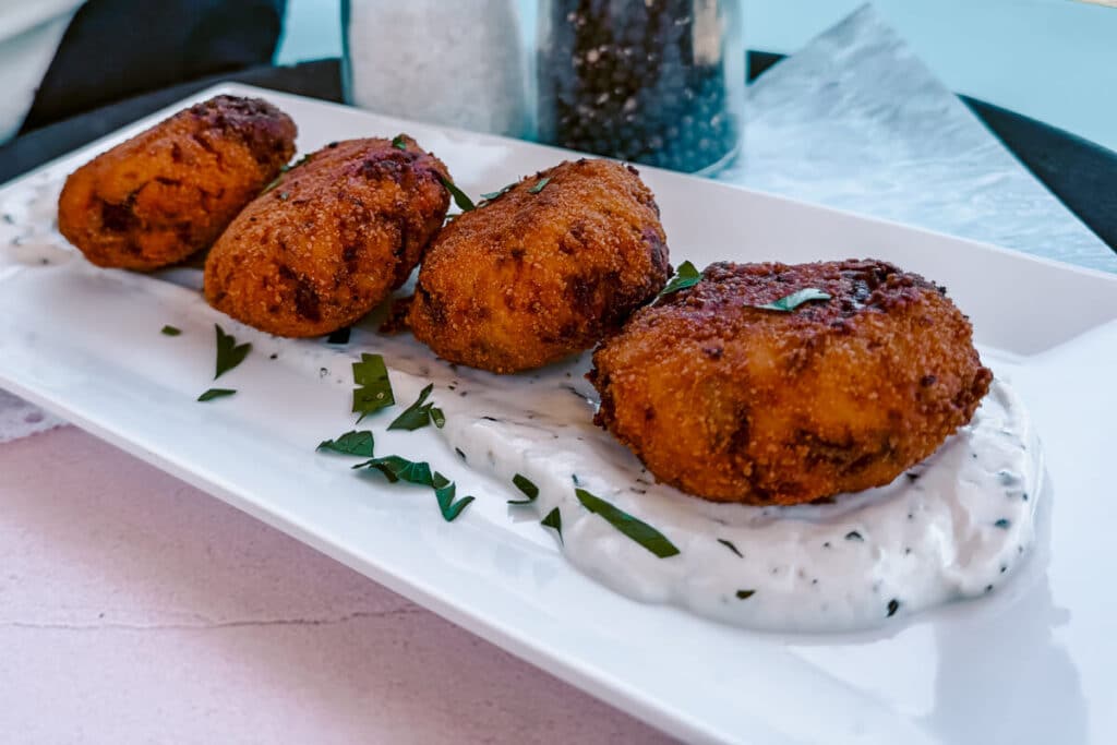 Golden fried croquettes served on a white plate with a creamy sauce at a restaurant in Paxos.