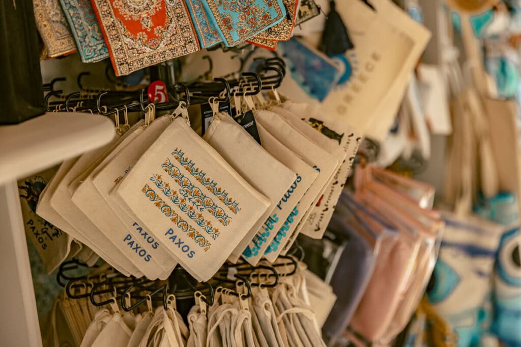 Souvenir shop display in Paxos with small fabric pouches, patterned textiles, and bags hanging on racks.
