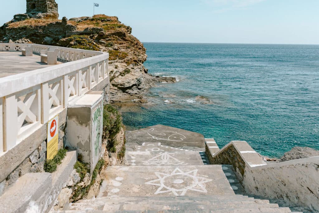 Stone steps near the old castle ruins in Chora, Andros, leading down toward the rocky coastline and blue sea.
