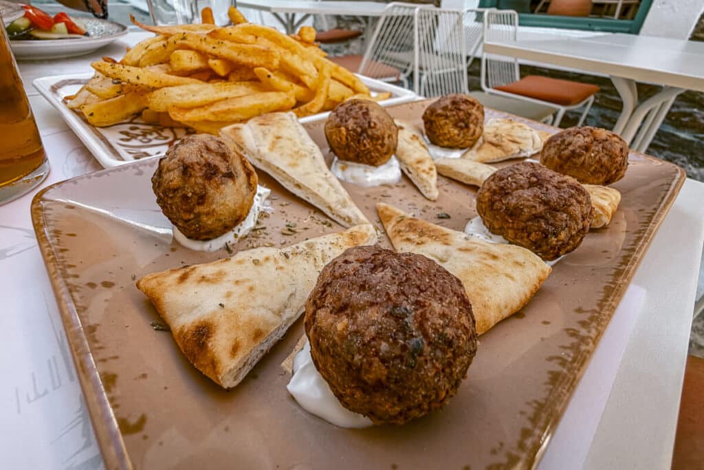 Greek meatballs served with pita, fries, and beer at an outdoor restaurant in Andros, Greece.