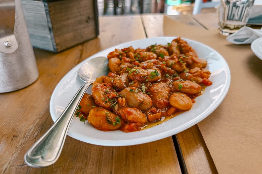 Plate of gigantes beans in tomato sauce on a wooden table at a restaurant in Andros, Greece.