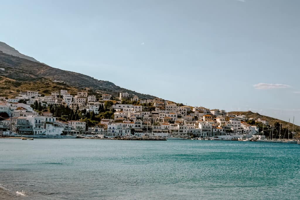 View of Batsi in Andros with white houses on the hillside, boats along the harbor, and calm turquoise water in the bay.