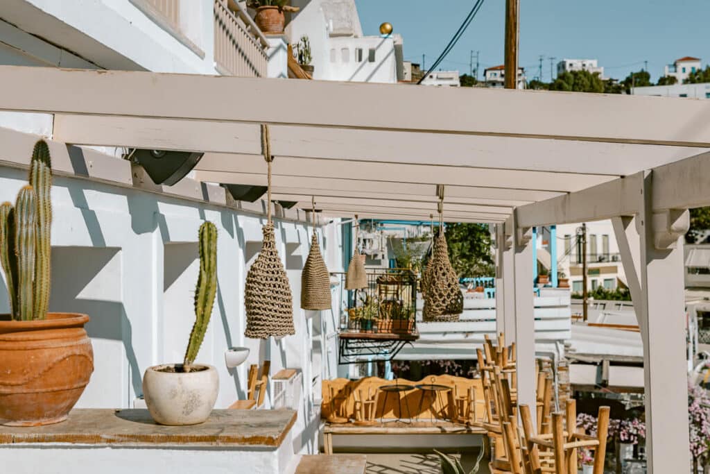 Outdoor cafe seating with woven hanging lamps, potted cacti, and white buildings in Batsi, Andros.