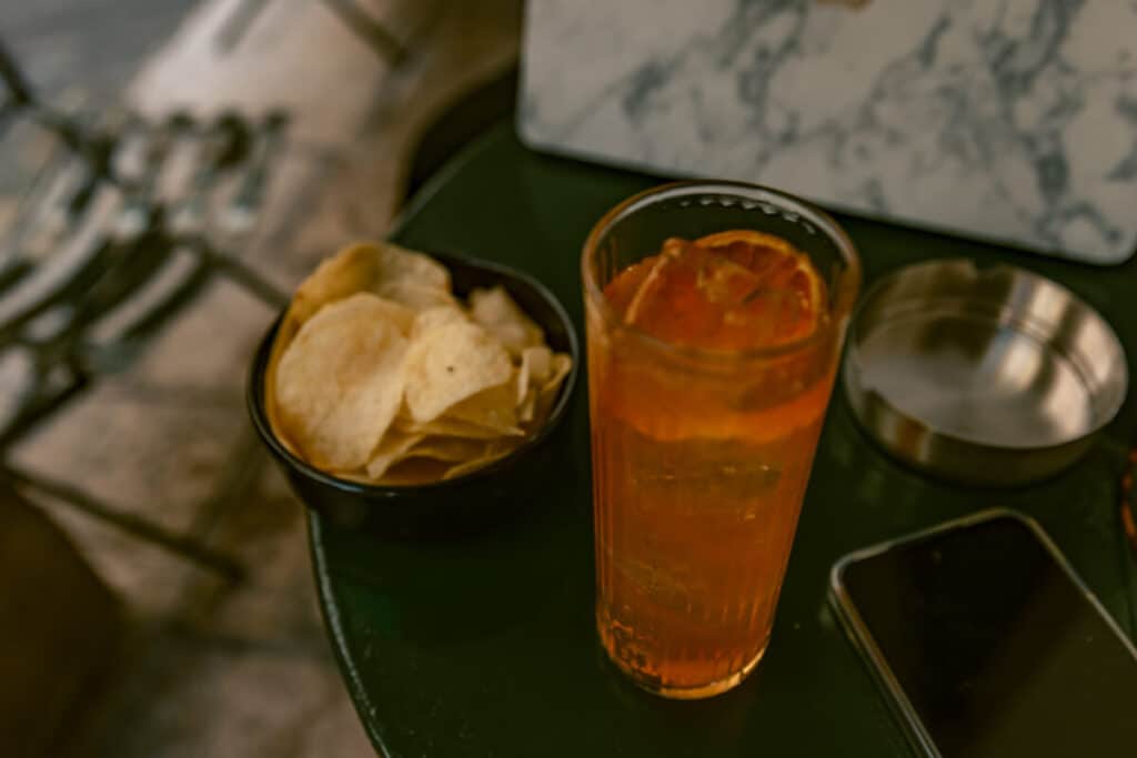 Kumquat cocktail served with potato chips on a small table at Mikro Café in Corfu Old Town.