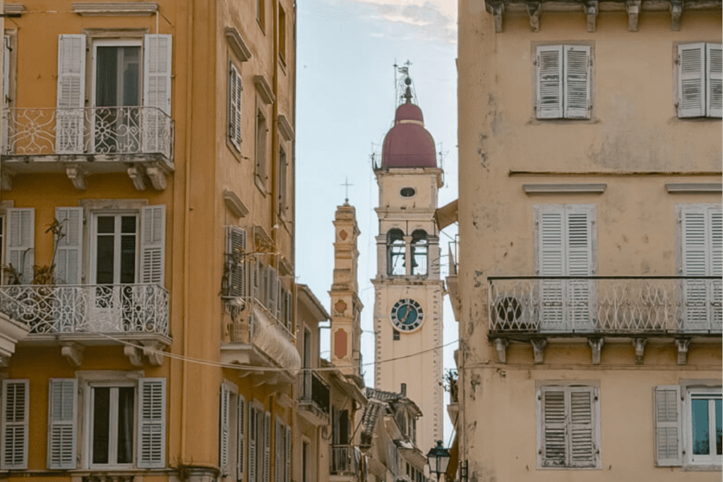 Bell tower of Saint Spyridon Church seen between pastel buildings with shutters and balconies in Corfu Old Town.