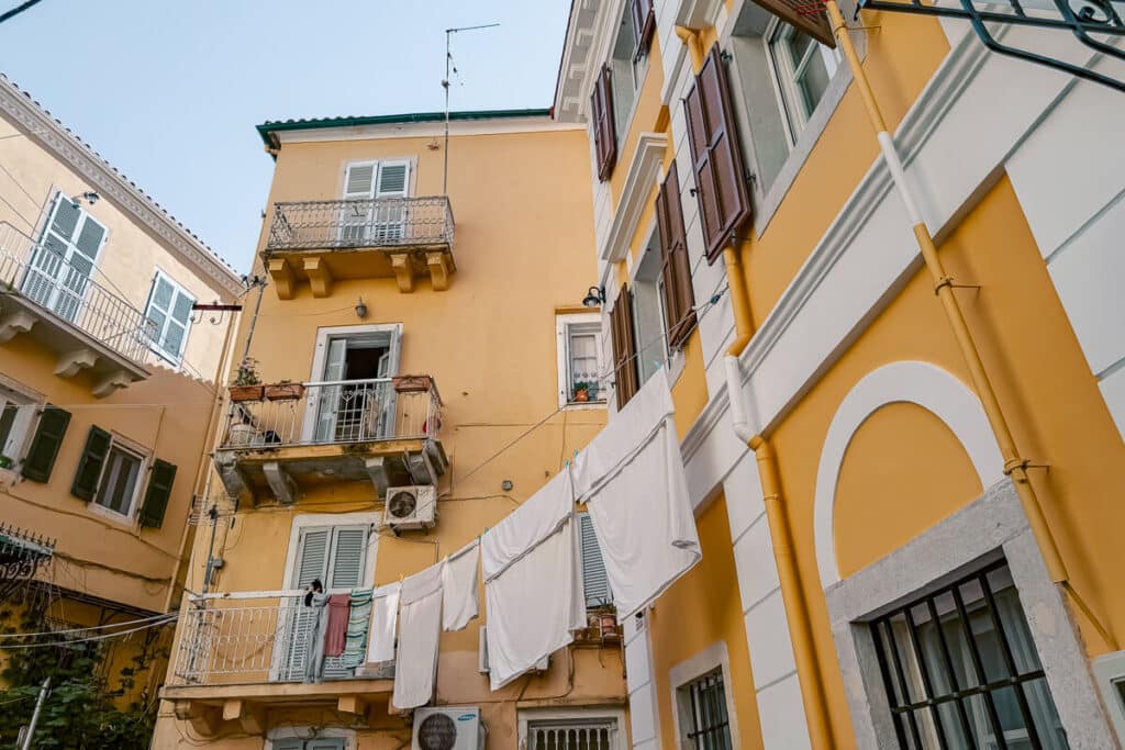 Yellow pastel buildings with balconies, shutters, and laundry hanging between windows in Corfu Old Town.