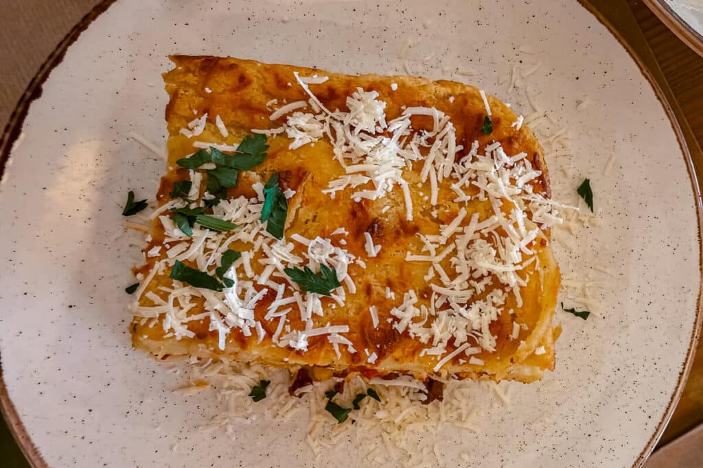 Pastitsio topped with grated cheese and parsley on a plate at Diporto in Corfu Old Town.