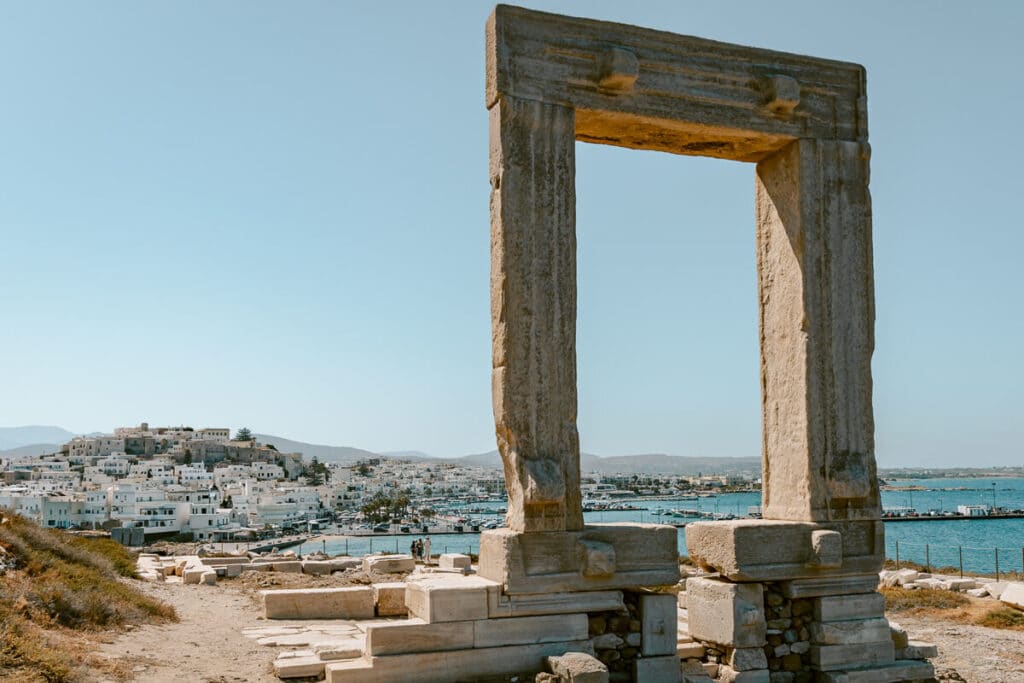The ancient Portara marble gateway overlooking Chora, Naxos harbor, whitewashed buildings, and the blue Aegean Sea on of the things to do in Naxos, Greece.
