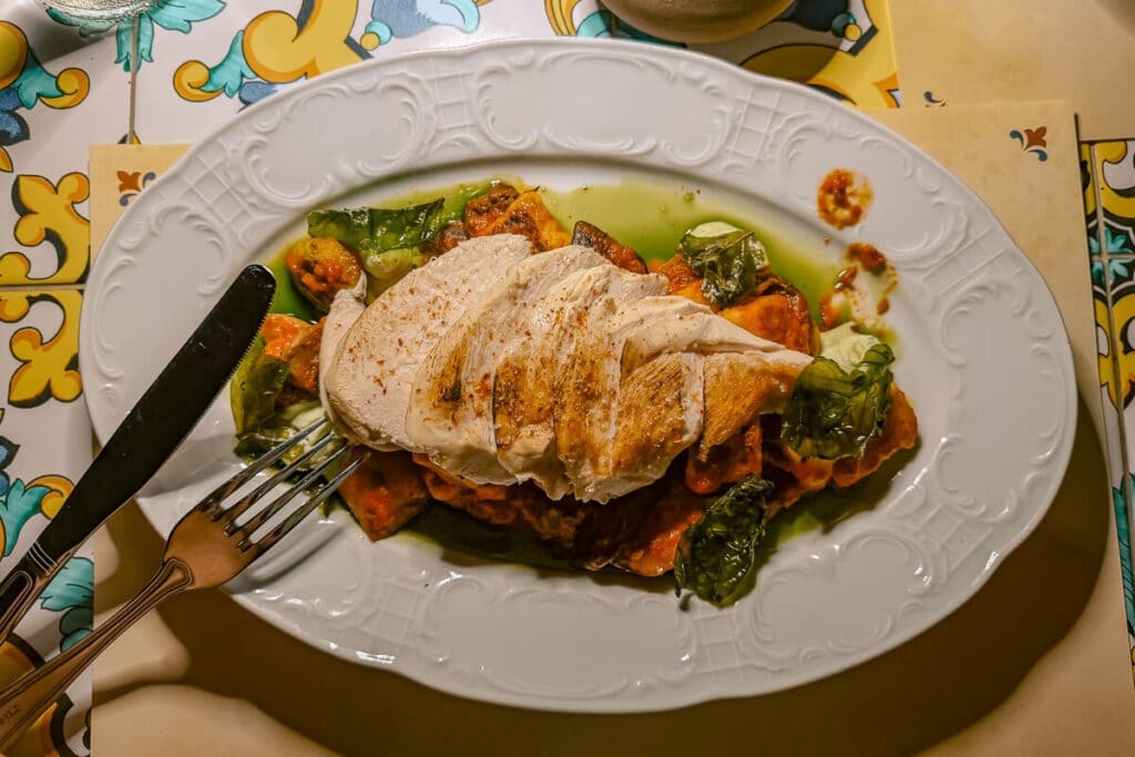 Sliced grilled chicken served over vegetables and tomato sauce on a white plate at a restaurant in Naxos.