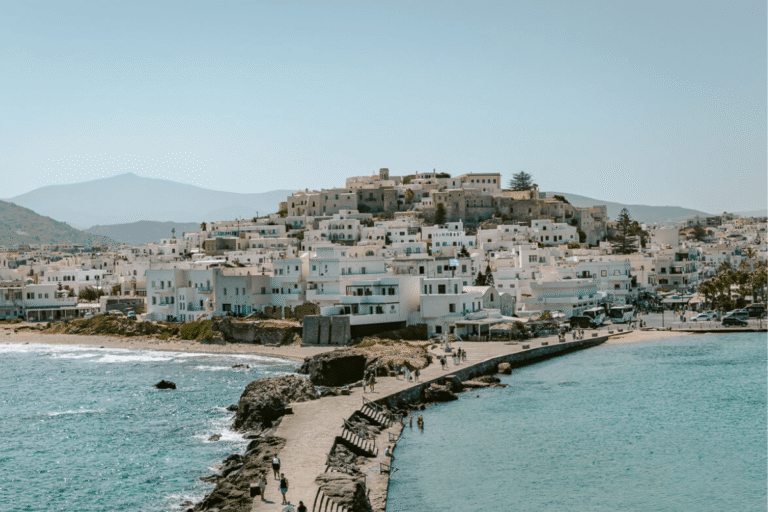 Whitewashed buildings of Naxos Town overlooking the turquoise Aegean Sea, a scenic highlight when exploring things to do in Naxos, Greece.