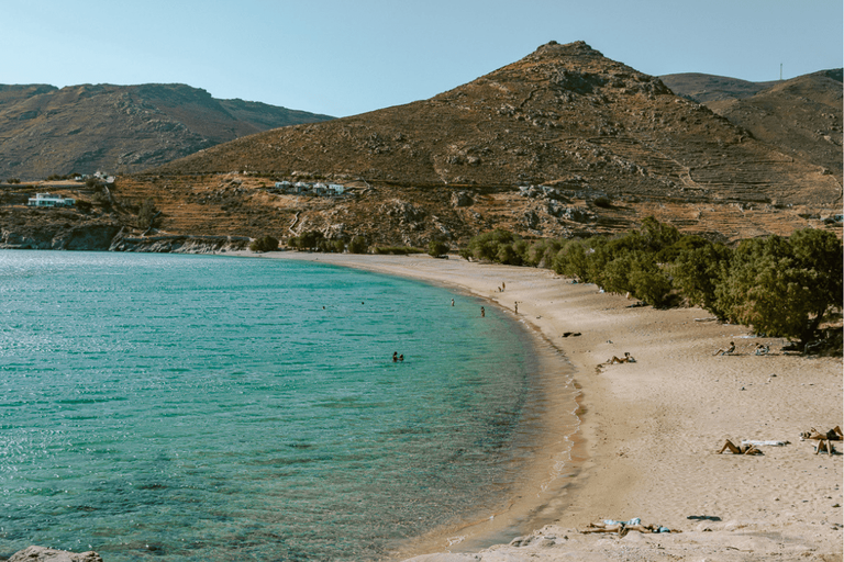 Ganema Beach, one of the Serifos beaches, with turquoise water, a sandy shoreline, sunbathers, tamarisk trees, and rugged hills in the background.