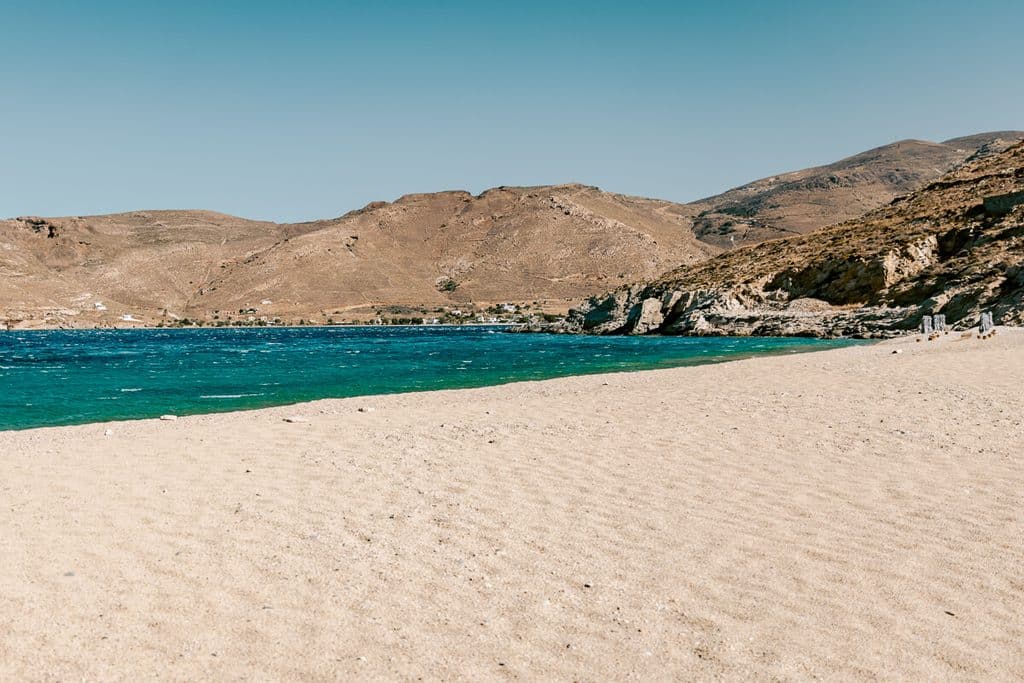 Vagia Beach in Serifos with a wide sandy shoreline, turquoise sea, rocky coastline, and dry rugged hills surrounding the bay.