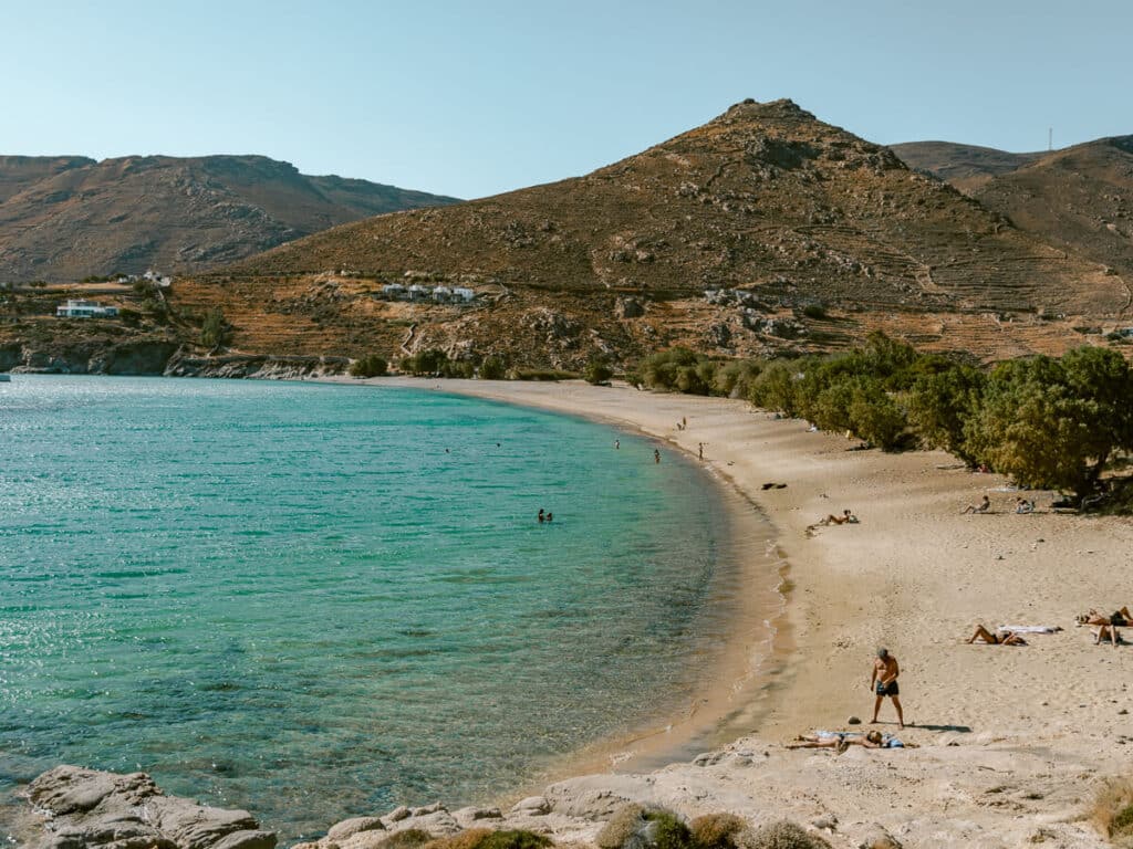 Sandy beach with clear turquoise water, swimmers, and dry rocky hills rising behind the shoreline in Serifos.